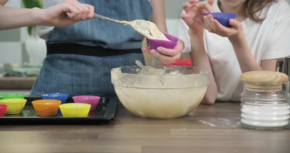 Close Up of Childrens Hands Pouring Dough Into Cupcakes