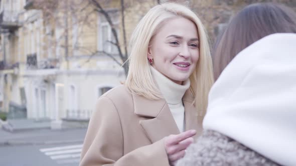 Close-up of Cheerful Blond Caucasian Girl Chatting with Friends Outdoors. Young Woman Talking and