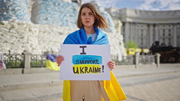 Woman Holds Placard Against Monuments Covered with Sandbags