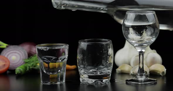 Pour Alcohol Vodka From a Bottle in Three Shot Glass. Background with Vegetables