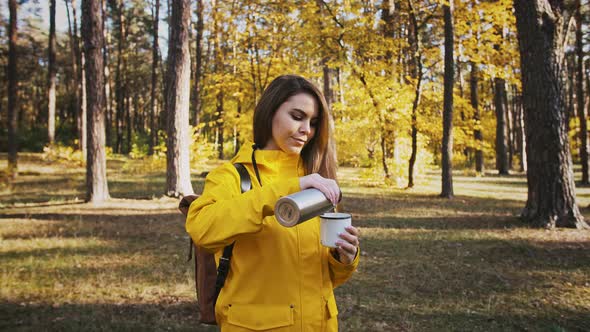 Young Woman is Pouring Hot Tea From Thermos Into a Mug Drinking It and Smiling Walk in Autumn Forest