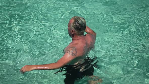 High Angle View of Tattooed Tanned Man Standing in Turquoise Mediterranean Sea in Sunshine