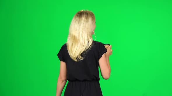 Blonde Girl in a Black Dress Walking and Drinking Coffee On, Shooting From the Back on a Green