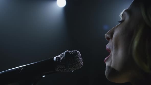 Close-up of the Face of the Singer with Microphone on a Black Smoky Background. The Singer Sings a