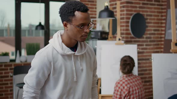 Male Teacher Looking at Elder Student Drawing on Canvas