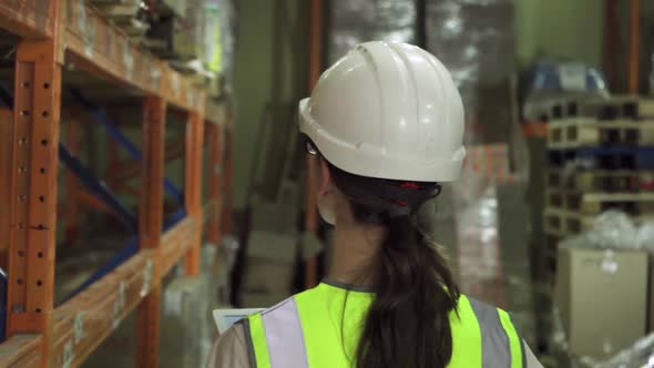 Back View of a Young Female Worker in a Protective Vest and Helmet As She Walks Through the