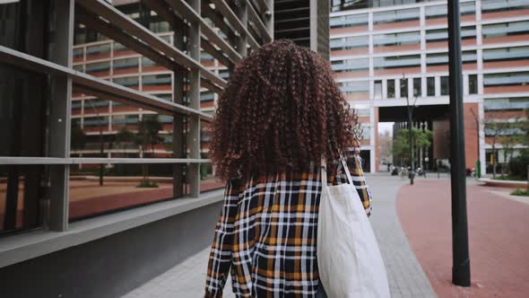 Back View of African American Girl with Curly Hair in Card Shirt is Going Home From the University