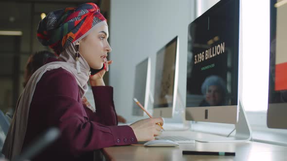 Businesswoman in Hijab Talking on Phone and Working on Computer