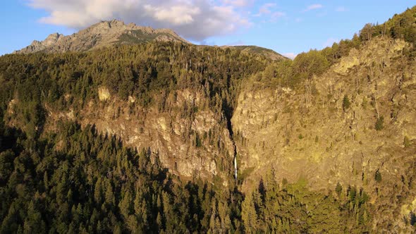 Aerial dolly out of pine tree forest mountains with Corbata Blanca waterfall flowing in background a