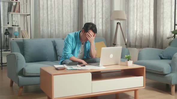 Asian Man With A Laptop Sitting On Sofa And Being Sad