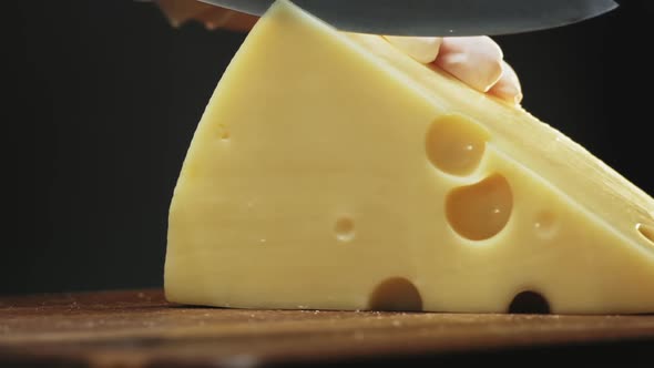 Person Cuts Tasty Hard Cheese with Large Holes on Board