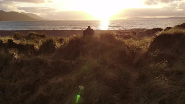 Flight Over a Young Couple Sitting on the Beach at Sunset – Very Romantic