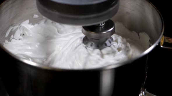 Electric mixer whipping cream in steel mixing bowl, close-up in slow motion
