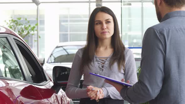 Young Woman Talking To the Salesman at the Car Dealership