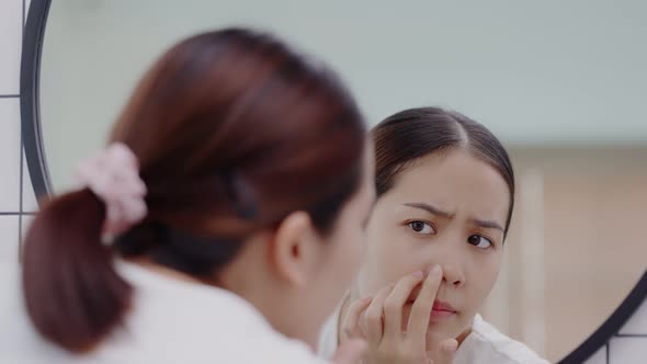 Happy Asian girl looking in to mirror worry about face skin problem.