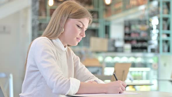 Serious Young Woman Doing Paperwork in Cafe