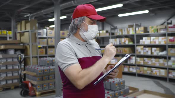 Aged Male Worker or Supervisor with Clipboard in Safety Mask at Warehouse