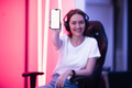 Smiling gamer girl wearing headset showing smart phone and pointing at blank screen with her finger - PhotoDune Item for Sale