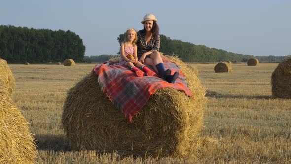 Mother with Little Daughter Sitting on a Hay Bale