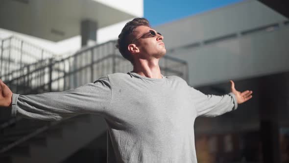 Handsome stylish white man in sunglasses raises his hands to the sides background city of a street