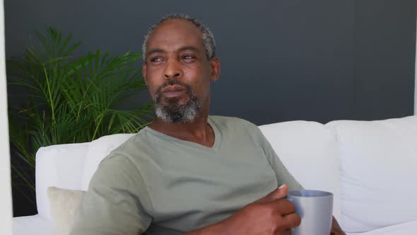 Senior african american man holding coffee cup while sitting on the couch at home