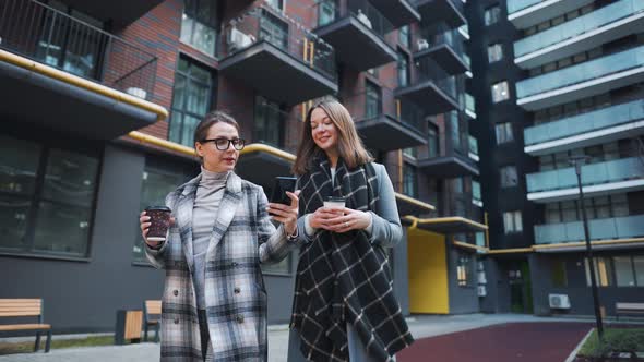 Two Happy Women Walking with Takeaway Coffee and Talking with Interest Among Themselves in the