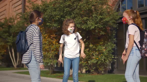 Three Schoolgirls in Safety Mask Bumping Elbows As Greeting Standing Outdoors