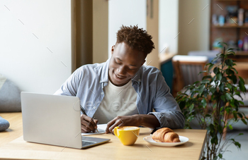 Happy black man studying remotely in front of laptop, taking notes during online class or lecture at / Photodune, Misc