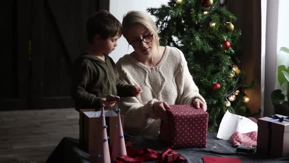 Mother with son wraps a Christmas gifts on a table