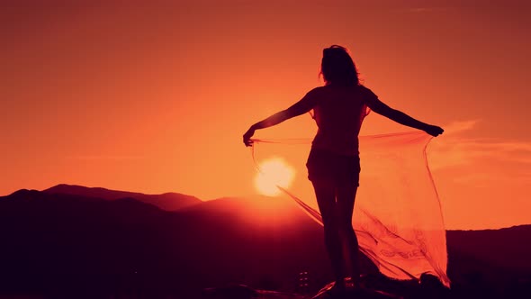 Young Woman with Hands Up Holding Scarf in Wind on the Mountain Landscape