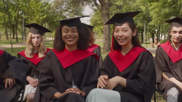 Smiling Multiethnic Female Students in Academic Dresses Expressing Happiness Outdoors