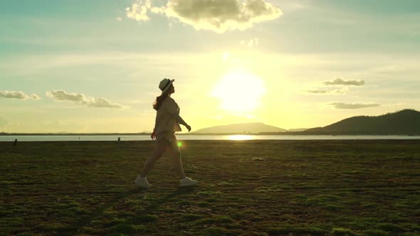 slow-motion of cheerful woman walking across the green field with sunlight