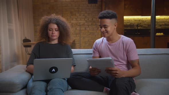 Young Mixed Race Couple Studying Online Together Sitting on Sofa at Home