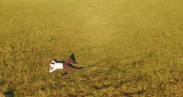 Low Orbital Flight Around Man on Green Grass with Notebook Pad at Yellow Rural Field