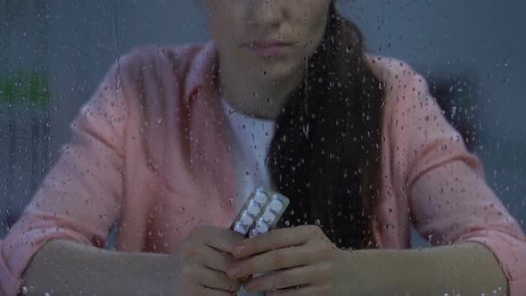 Depressed Lonely Female Holding Blister Pack of Pills Near Rainy Window, Disease