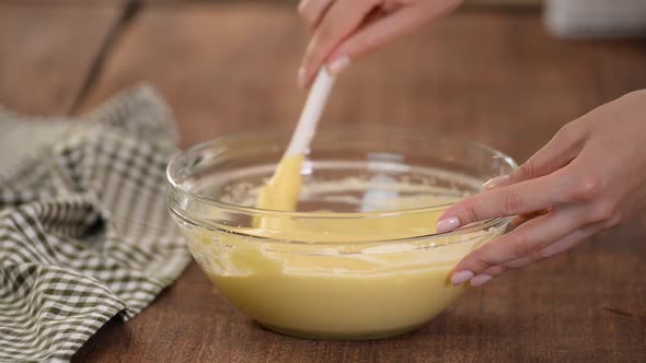 Baker Hands Stirs the Dough with a Spatula in a Glass Bowl.