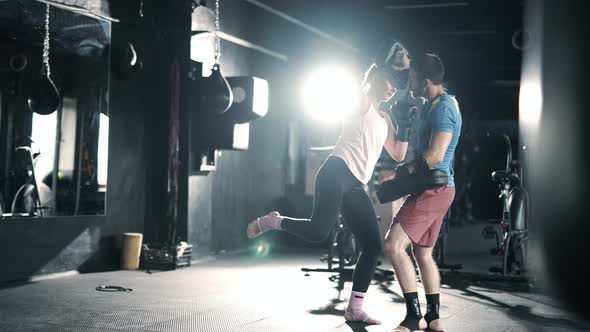 A Athlete Woman Fighter is Training Punches Focus Mitts in the Dark Gym