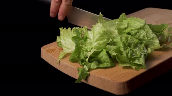 Hand with a kitchen knife and sliced lettuce on a wooden cutting board 