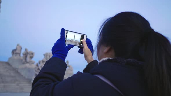 Back view of Asian woman standing and taking a photo in public Frogner park, Norway