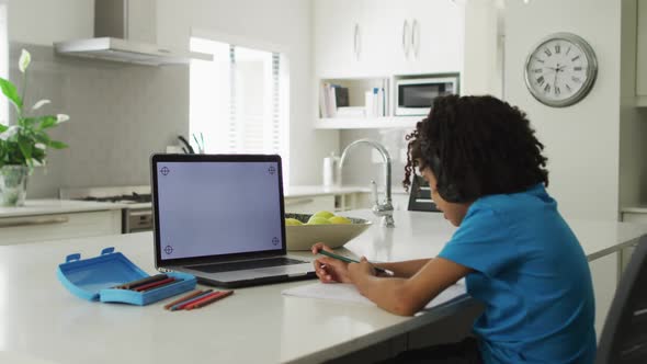 Happy biracial boy sitting at table using laptop with copy space and having online classes