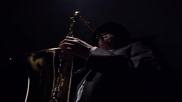Male Saxophonist Playing a Saxophone with Hands and Mouth is Caught in the Light From Above in a