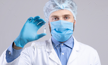 Vaccination and health protection. Male doctor in facial mask holding vaccine or medication on grey / Photodune, Misc