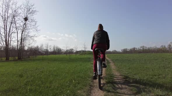 Young Woman on a Bicycle Rides Along a Path in the Forest in a Sunny Spring Day