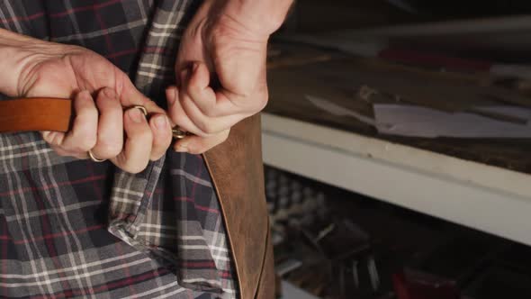 Close up of hands of caucasian male knife maker in workshop tying apron