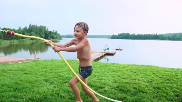 Boy in Summer Swimming Trunks Pours Water on His Younger Brother Having Fun in the Park on the Grass
