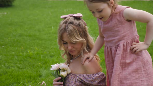 Daughter Hugs Her Mother Sitting on a Green Meadow in Summer in Nature