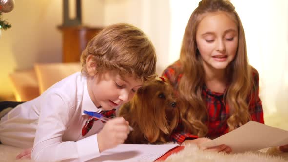 Concentrated Little Boy Writing Letter to Santa with Blurred Girl and Puppy at Background