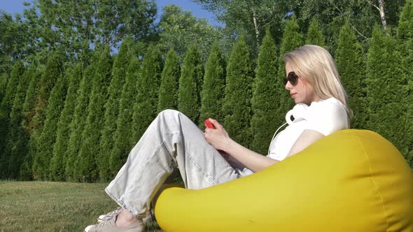 Woman sitting in soft chair and using mobile phone in a garden