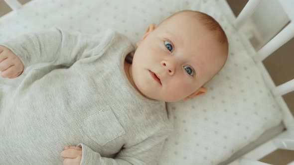 Top View of the Little Newborn Baby Lying on the Cot and Looking at the Camera