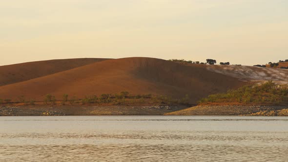 Desert like hill landscape with reflection on the water on a dam lake reservoir at sunset